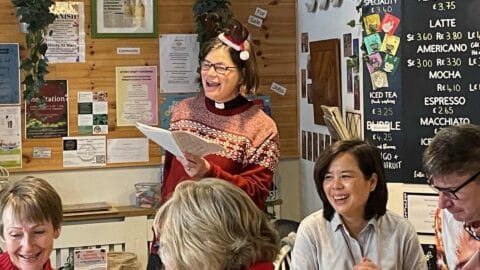 A picture of Lydia, in a Christmas jumper and antlers, leading the community carol singing in The Coffee Bank in Ottery St Mary
