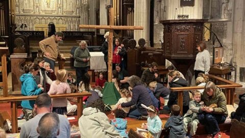 Families gathered around the big wooden cross in the nave at the Easter Experience, making wooden crosses out of sticks to lay a the base of the cross