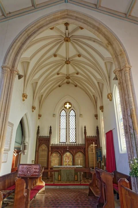 A view down Escot church to the altar also showing ceiling detail of stone arches and gold ceiling bosses