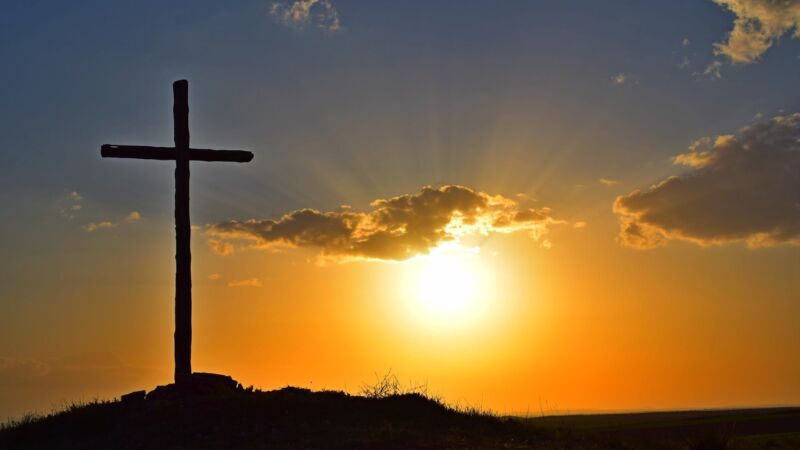 A cross on a hill with the sun setting behind