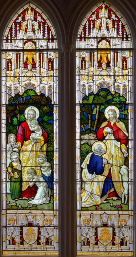 A view of a stained glass window at Tipton St John church depicting Jesus welcoming children and giving Peter his commission