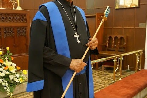 A verger in verger gown with wand