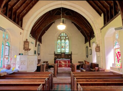 A view inside Venn Ottery church looking east at the altar showing pine pews and a carved stone pulpit