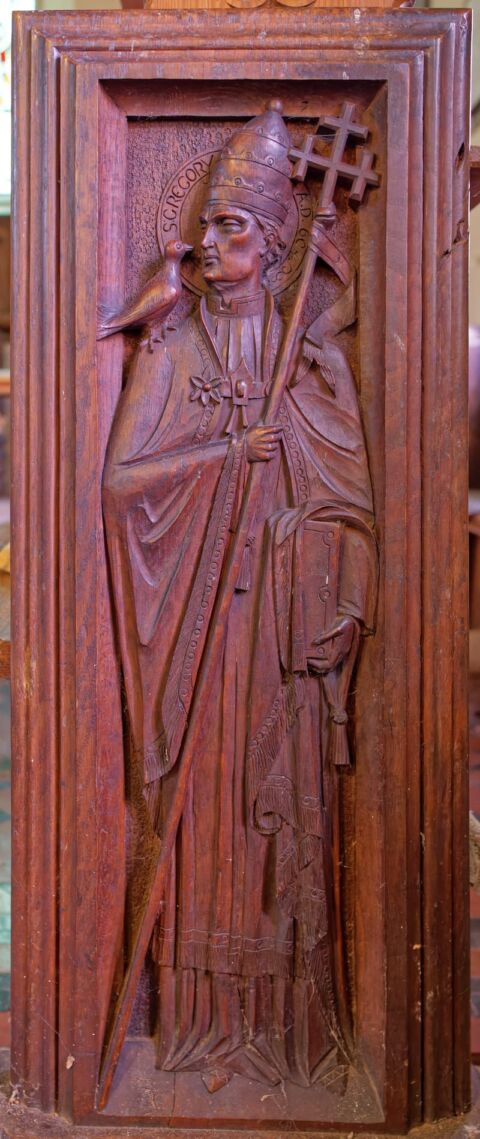 A view of a carved wooden pew end showing St Gregory holding a staff and with a dove on his shoulder