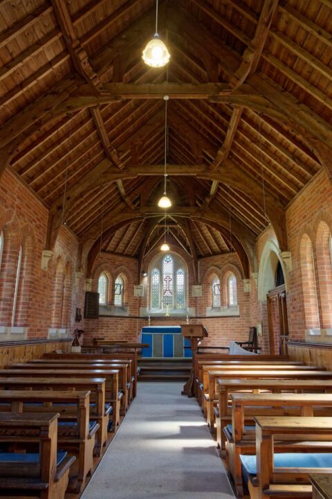 A view inside Wiggaton church looking east down the nave towards the altar and showing the brick walls and wooden ceiling